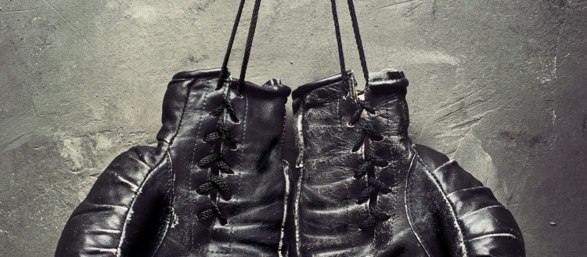 Black boxing gloves hanging on a nail on gray wall